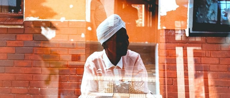 African woman seated inside behind a window with reflections all around her - what is my purpose she asks?