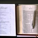 You Need Training as a Pastor: Image of book of doctrines, the bible open to Acts with a pen and stack of books