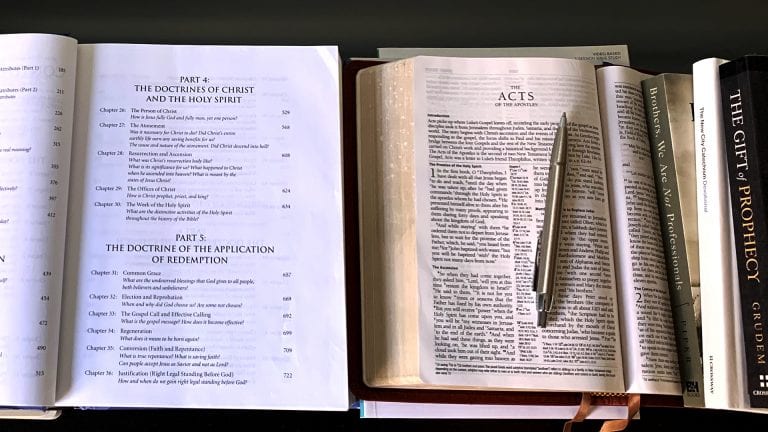 You Need Training as a Pastor: Image of book of doctrines, the bible open to Acts with a pen and stack of books