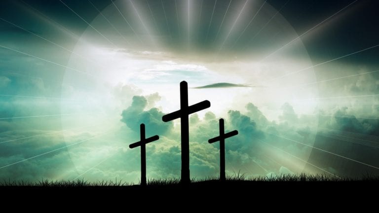 Three Crosses on a hill at dusk - surrounded by a glow of light - silhouetted against a cloud filled sky