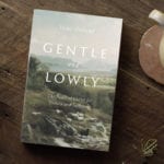 Gentle and Lowly book on a wooden table top with coffee and candle