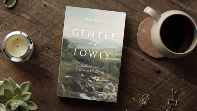 Gentle and Lowly book on a wooden table top with coffee and candle