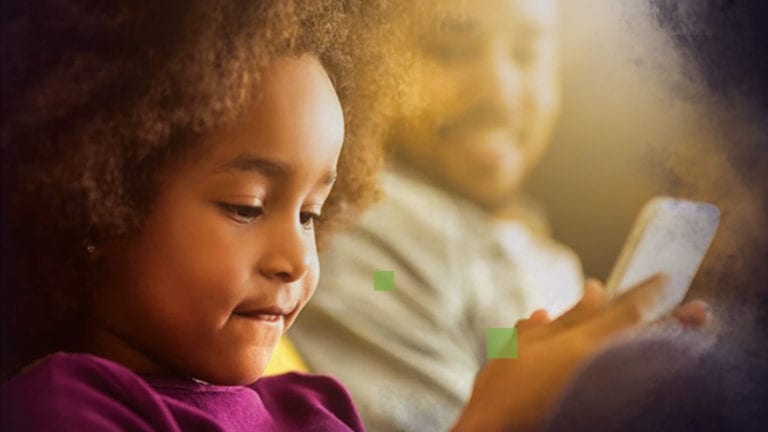 Parenting and the internet - cute African girl on a smart phone with Dad in the background
