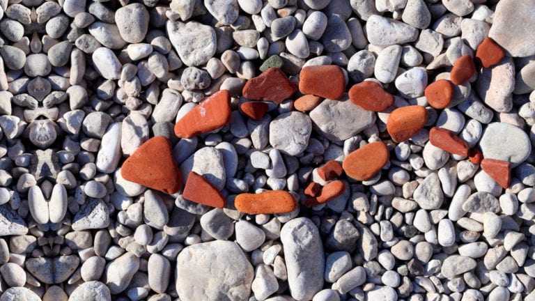 Christian Fish symbol in red stones on grey pebbles - contrast of faith and culture