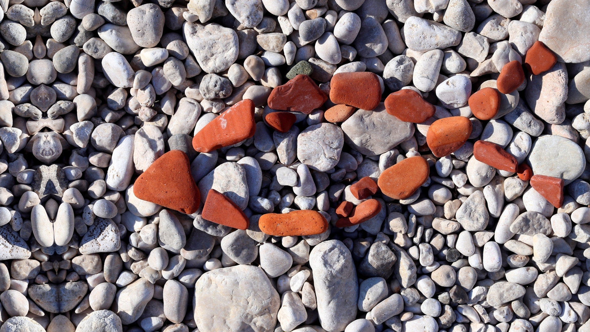 Christian Fish symbol in red stones on grey pebbles - contrast of faith and culture