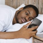 African man in bed gazing at his phone. The affect of social media on our spiritual growth can be negative.