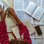 What's Your Story? African woman writing notes in a book lying on a surface of books.