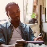 African man listening to a sermon and taking notes in a cafe