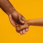 An authentic relationship with God: African child holding African father's hand with mustard colour block background