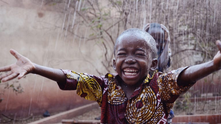 Africa is blessed not cursed! Small African boy grinning in the rain