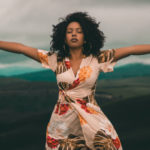 Living God's way - A woman standing in nature with her arms and hands wide open.