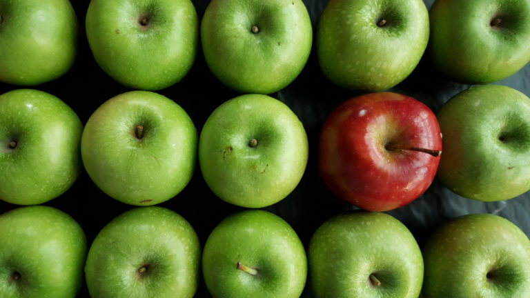 Being a Christian in the world - Green apples in a row with one red apple amongst them