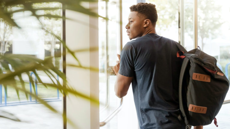 Campus - An African student walking out the front door of a university with backpack on