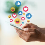 Social media - A guy holding a phone with emoticons floating around the phone