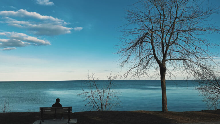 Waiting on God - A guy sitting on a bench looking out over the ocean