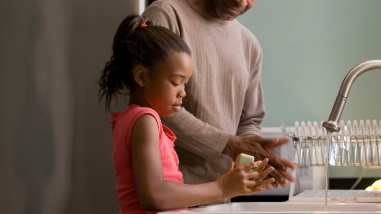 God our father and earthly father - A girl washing her hands with her father in the background