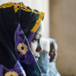 Child marriage - A girl sitting against a wall, staring at the ground.