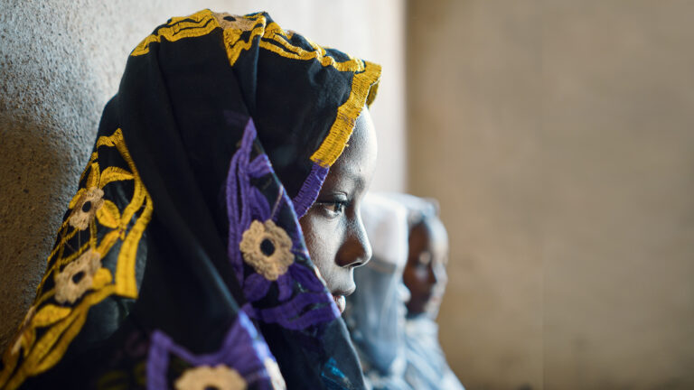 Child marriage - A girl sitting against a wall, staring at the ground.