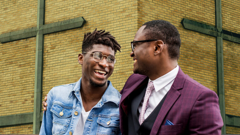 Spiritual Fathers – A man standing next to another man, giving him a side hug.