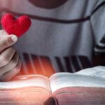 Pastors and character – A man sitting in front of an open bible holding a cushioned heart in his hand