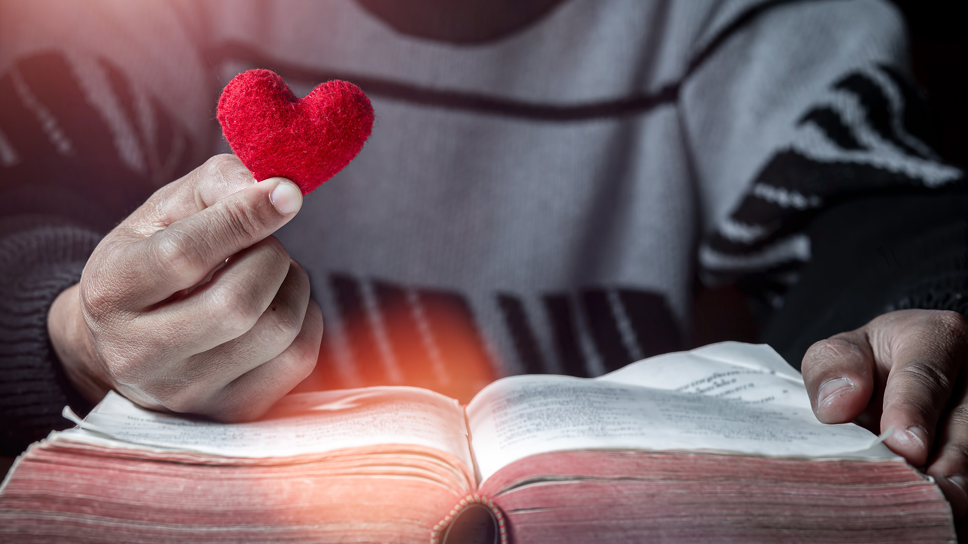 Pastors and character – A man sitting in front of an open bible holding a cushioned heart in his hand