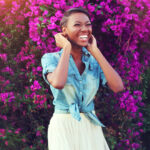 Being a woman of God – A lady standing in front of a purple bush of flowers, smiling