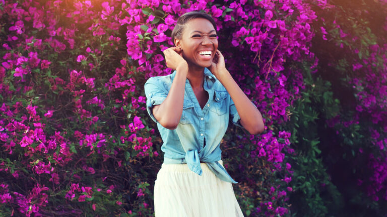 Being a woman of God – A lady standing in front of a purple bush of flowers, smiling