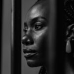 Singleness – A woman standing behind bars looking out into the distance